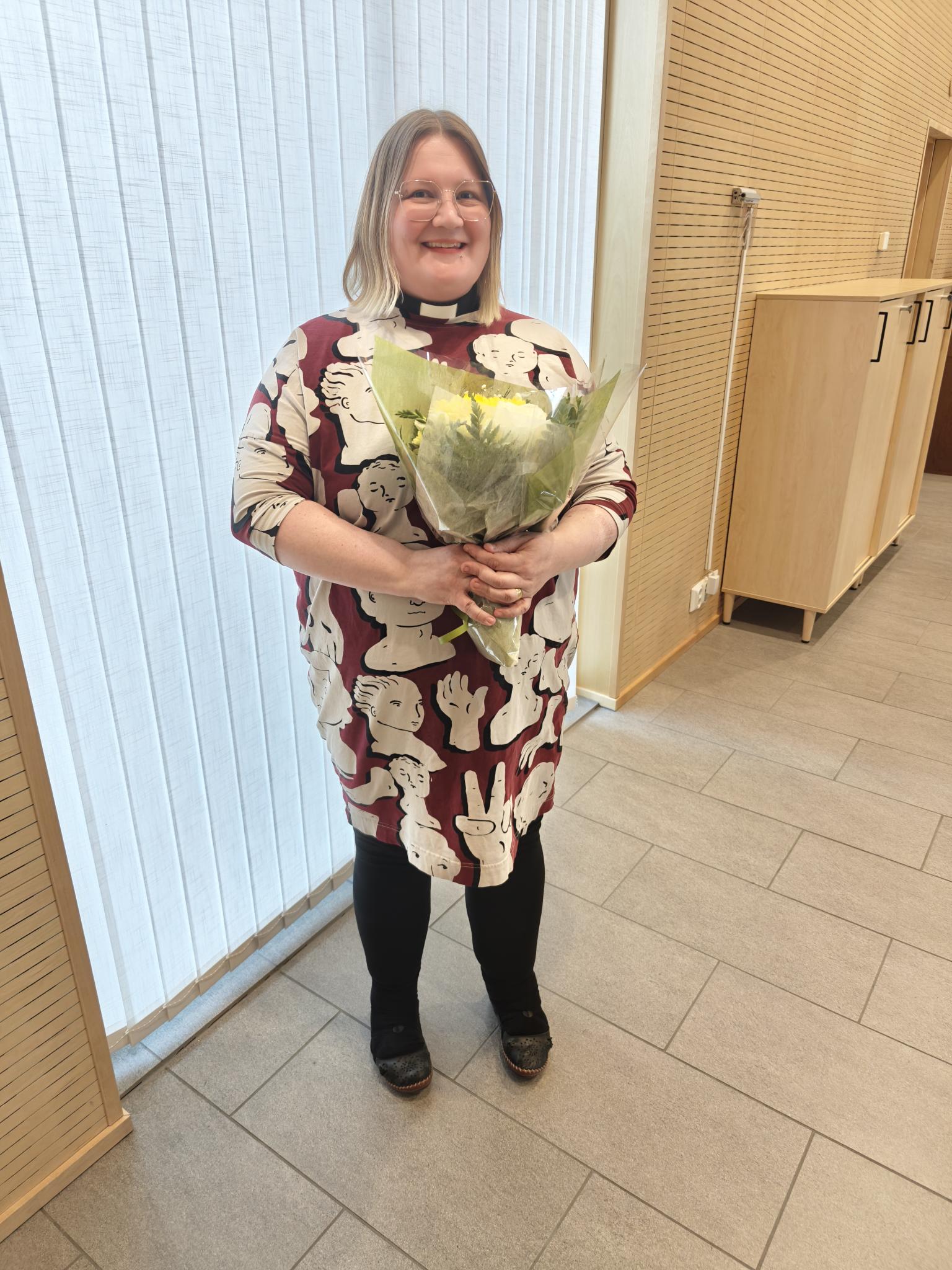 Tiina Keinänen seurakuntatalolla, kukkakimppu kädessään.