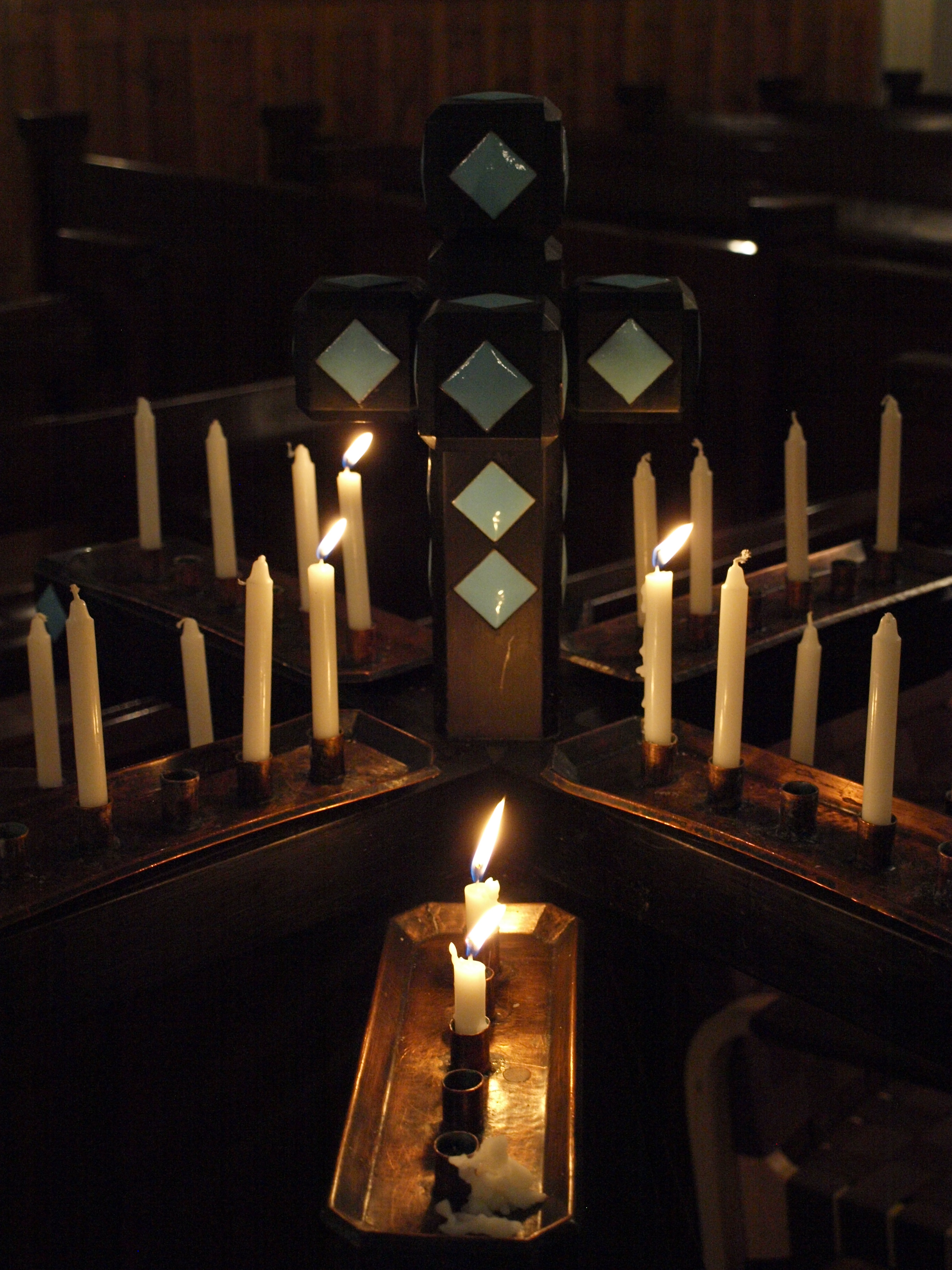 Tummasävyinen kuva lähetyskyntteliköstä, jossa osa kynttilöistä palaa.